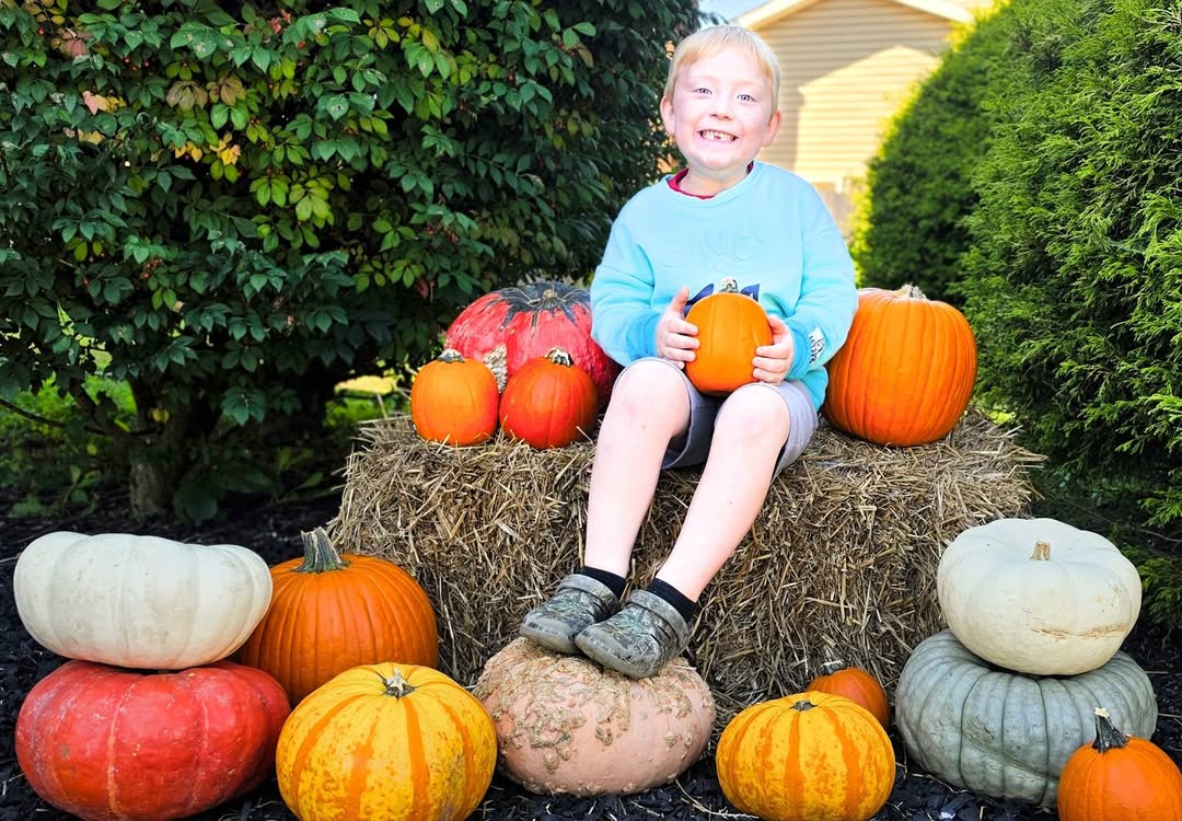 Student smiling on a hay bale with pumpkins